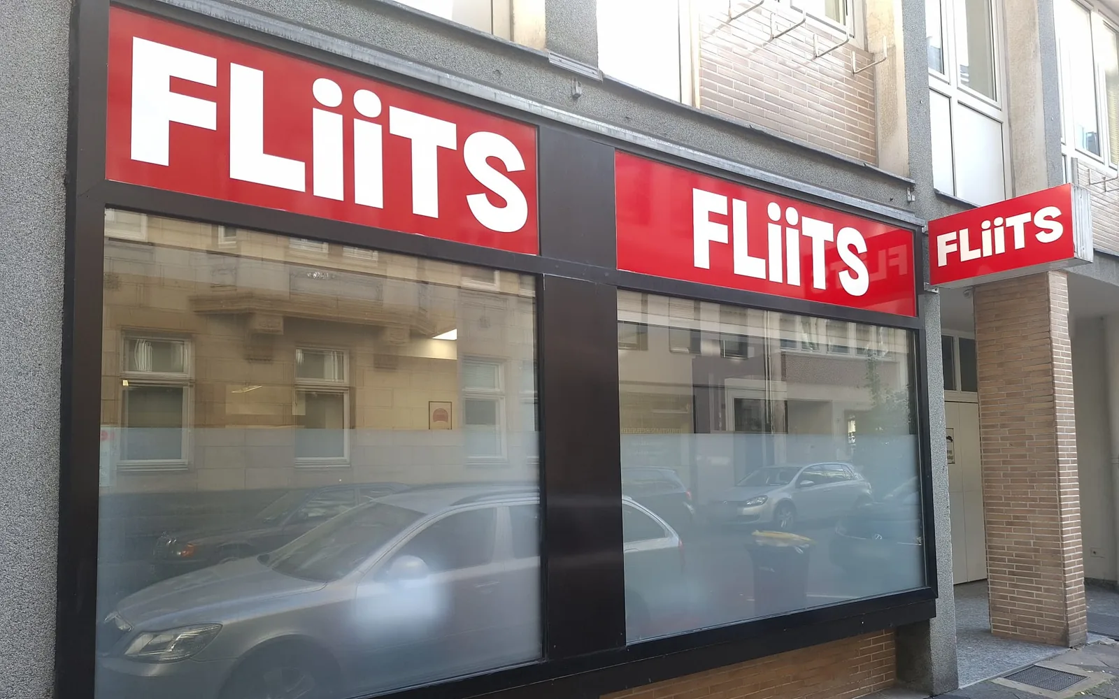 Façade of the FLiiTS office in Düsseldorf: two red panels with the white FLiiTS wordmark above the shop windows and a lettered light box